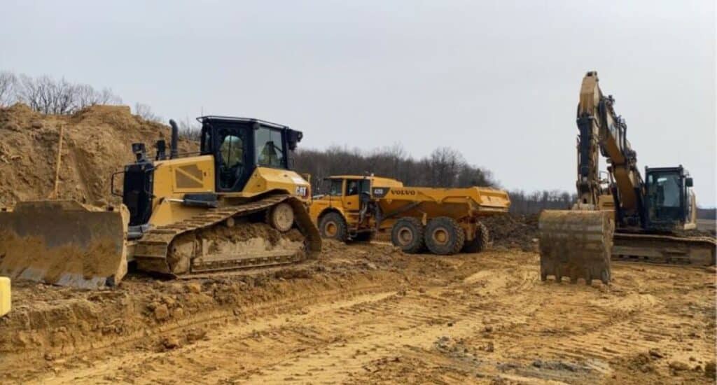 Engins de chantier : Bulldozer, excavatrice et tombereau Bulldozer CAT, tombereau Volvo et excavatrice sur un chantier de terrassement en plein air.